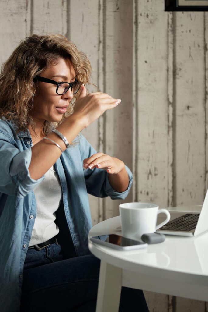 Eine Frau mit Brille und Hemd sitzt an einem Tisch mit einem Laptop.